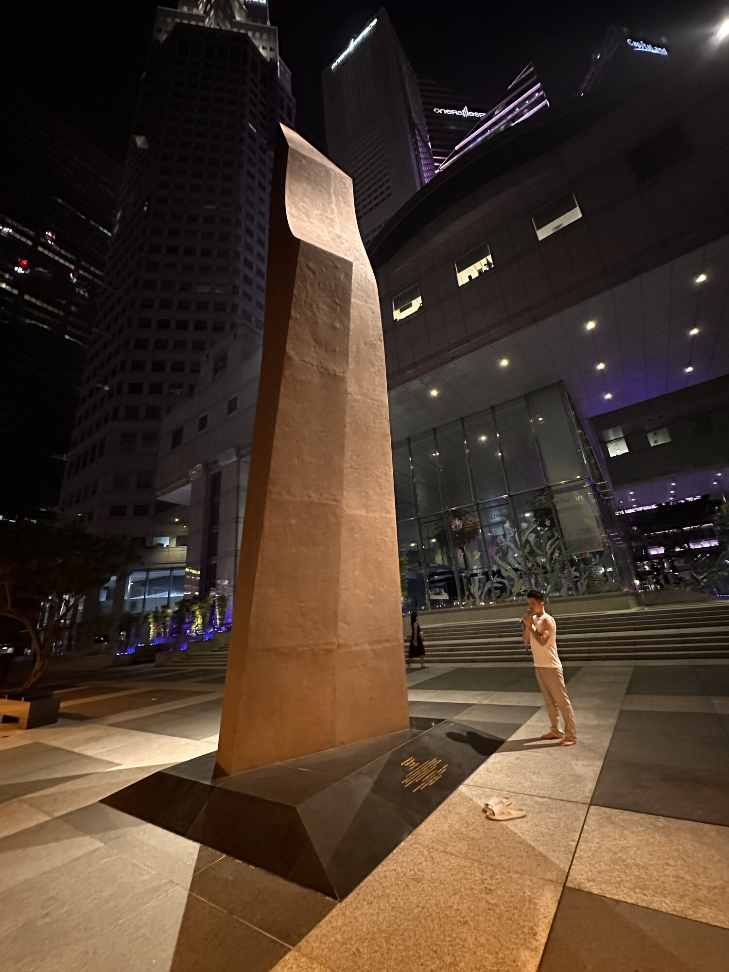 A person beside a tall, curved sculpture at night.