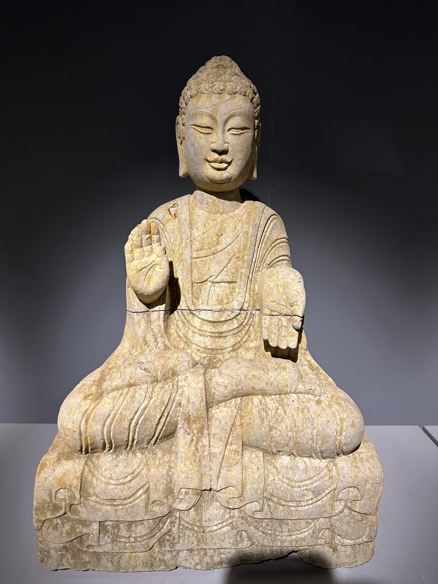 A seated stone figure with visible face and palms against a dark background.