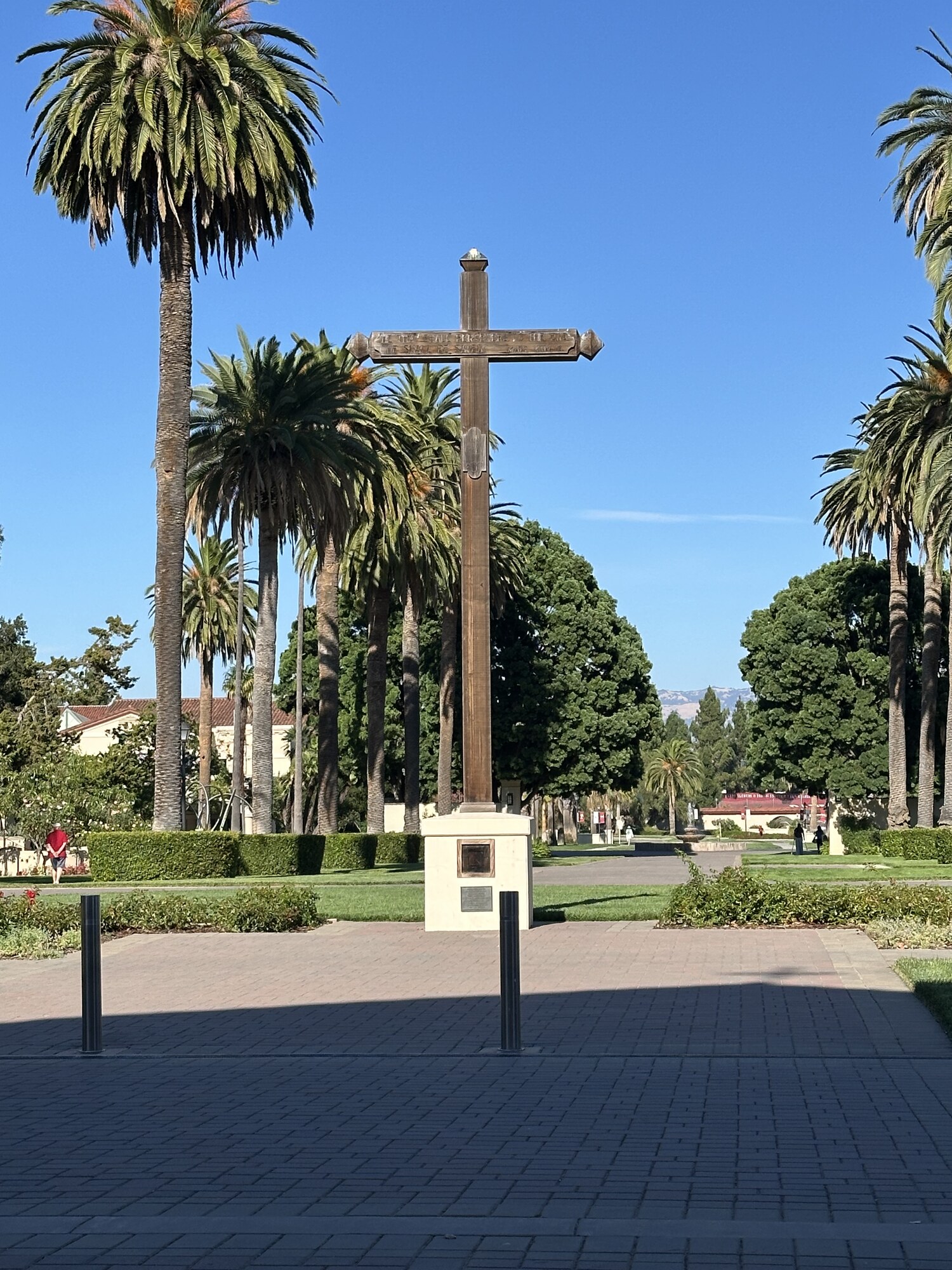 A cross standing between rows of palm trees.