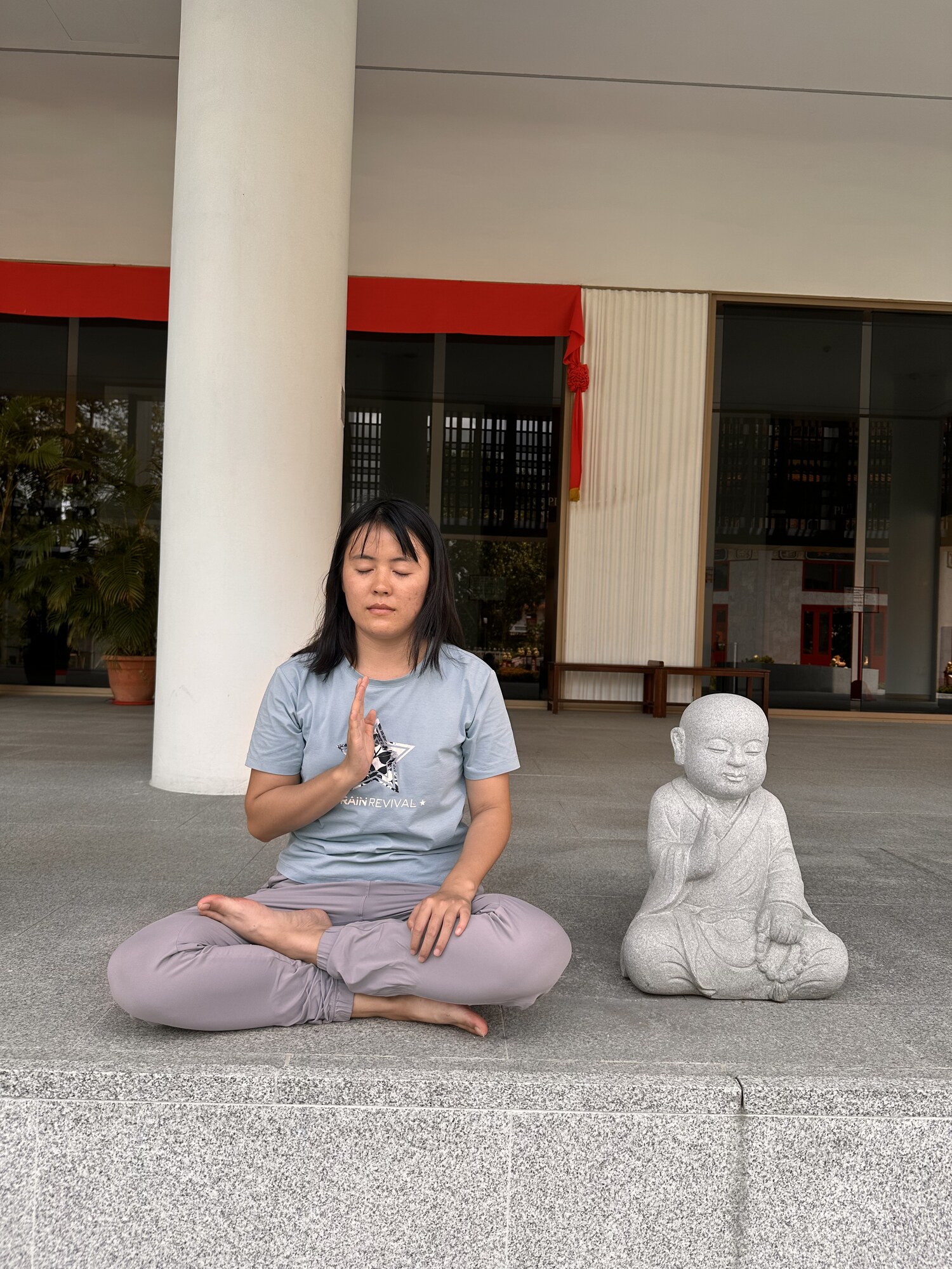 A person sitting cross-legged beside a small stone figure.