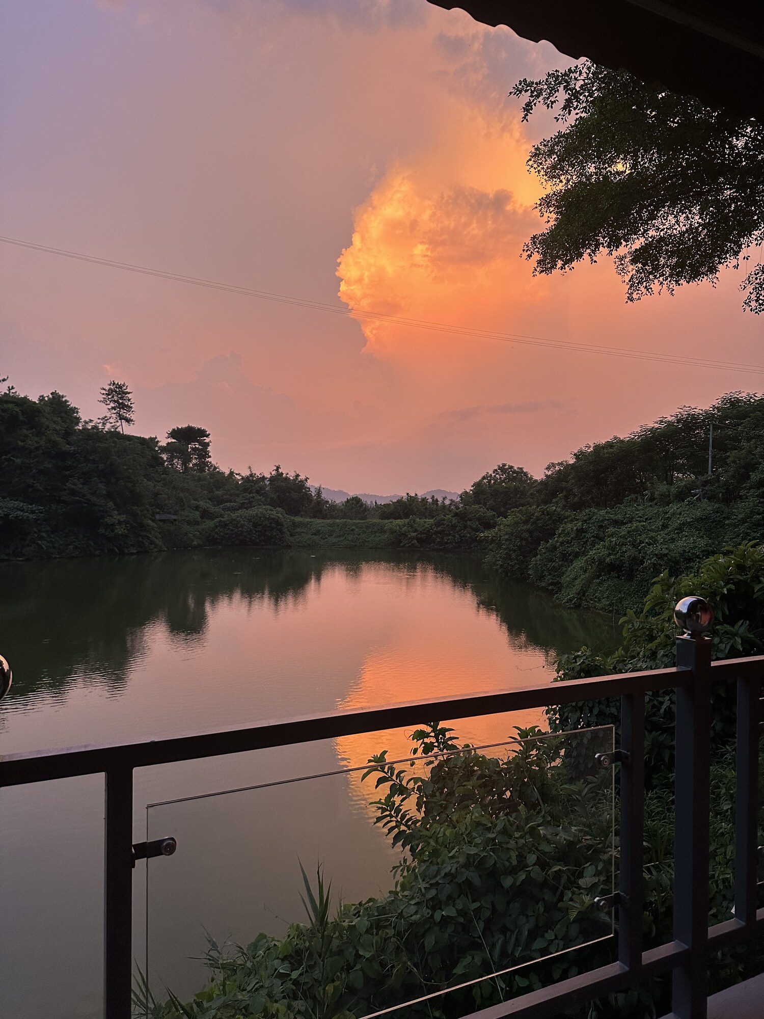 An orange cloud reflected in water beyond a railing.