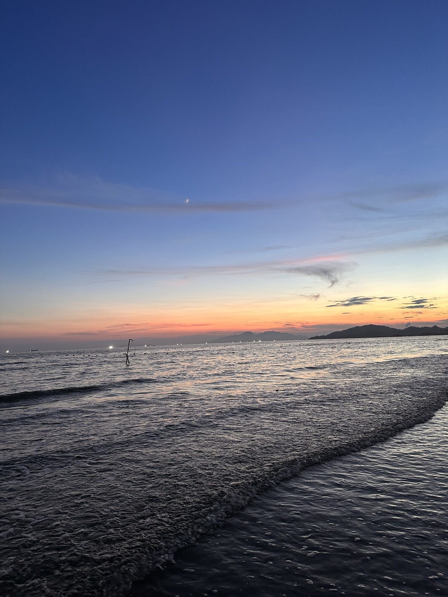 Small waves along a quiet beach beneath a pale evening horizon.